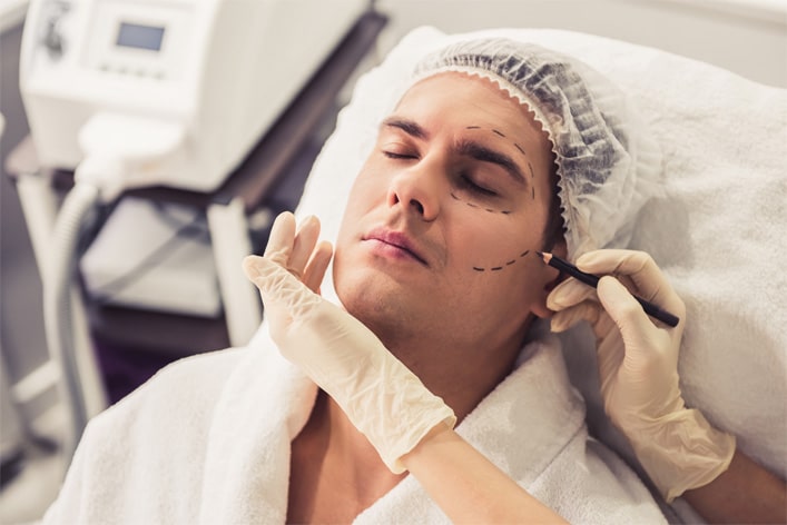 Handsome man is sitting at the cosmetician while doctor in medical gloves is examining his face using a pencil