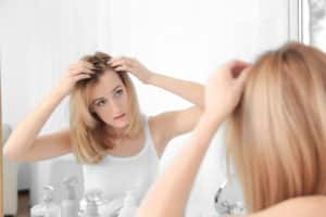 woman with hair loss problem looking in mirror at home