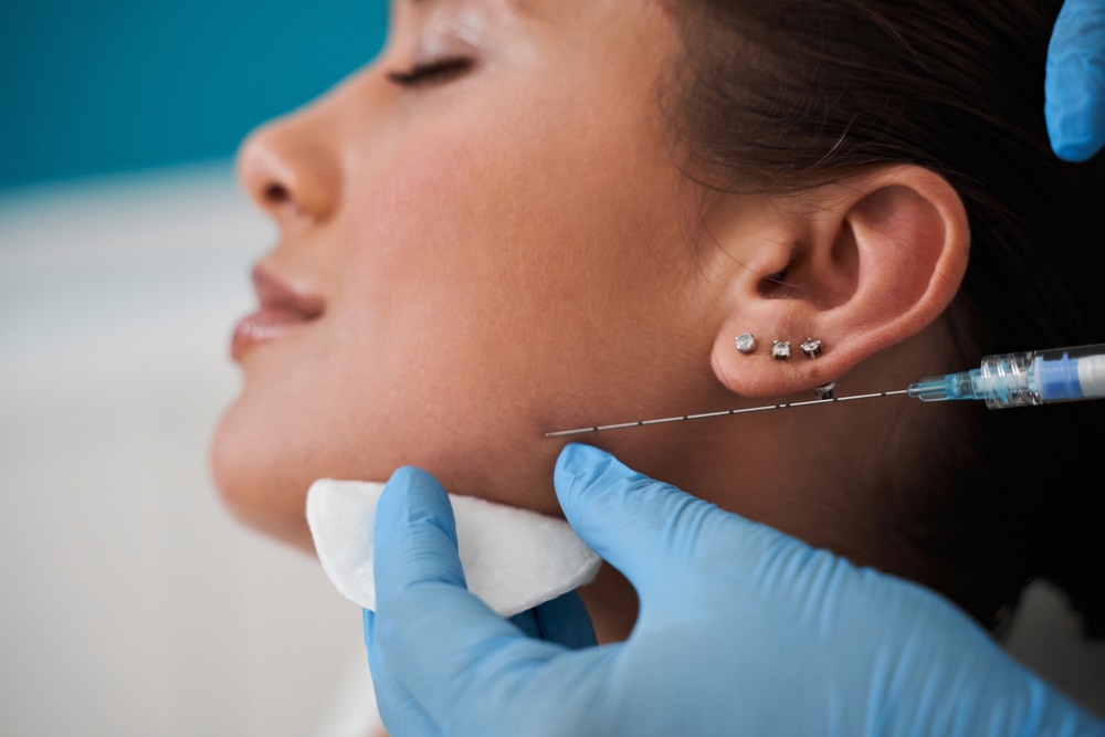 Woman receiving a botox injection in the chin zone while lying on the medical couch
